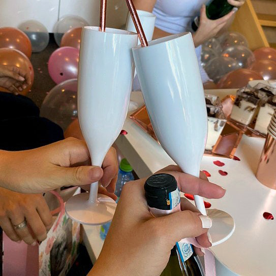 White plastic prosecco flutes held by two women surrounded by hen party decorations