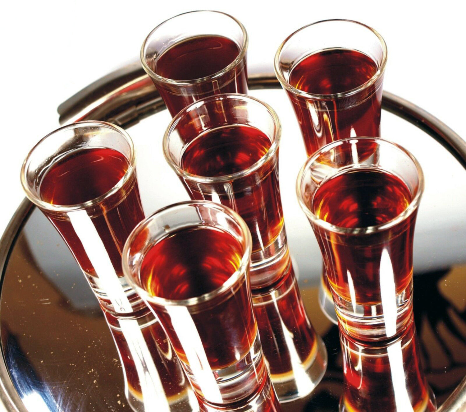 A mirrored tray with 6 clear plastic shot glasses on filled with a dark beverage