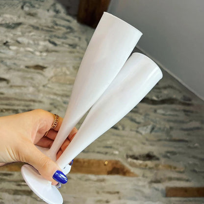 Two white plastic champagne flutes being held by a woman with blue nail vanish and a gold ring on her finger