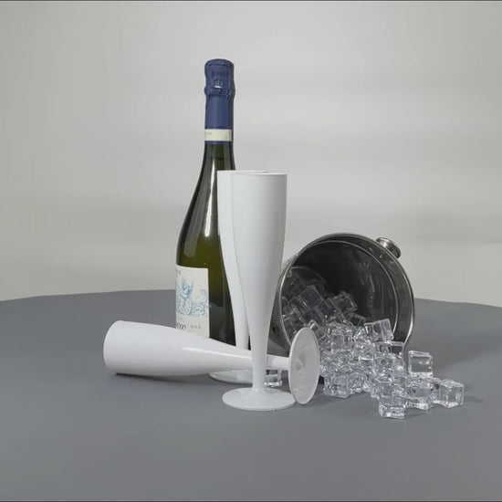 a video of a group of white disposable plastic flutes sitting next to a bottle of prosecco and an ice bucket which is tipped over and ice is falling out. The table is grey and the video is spinning 