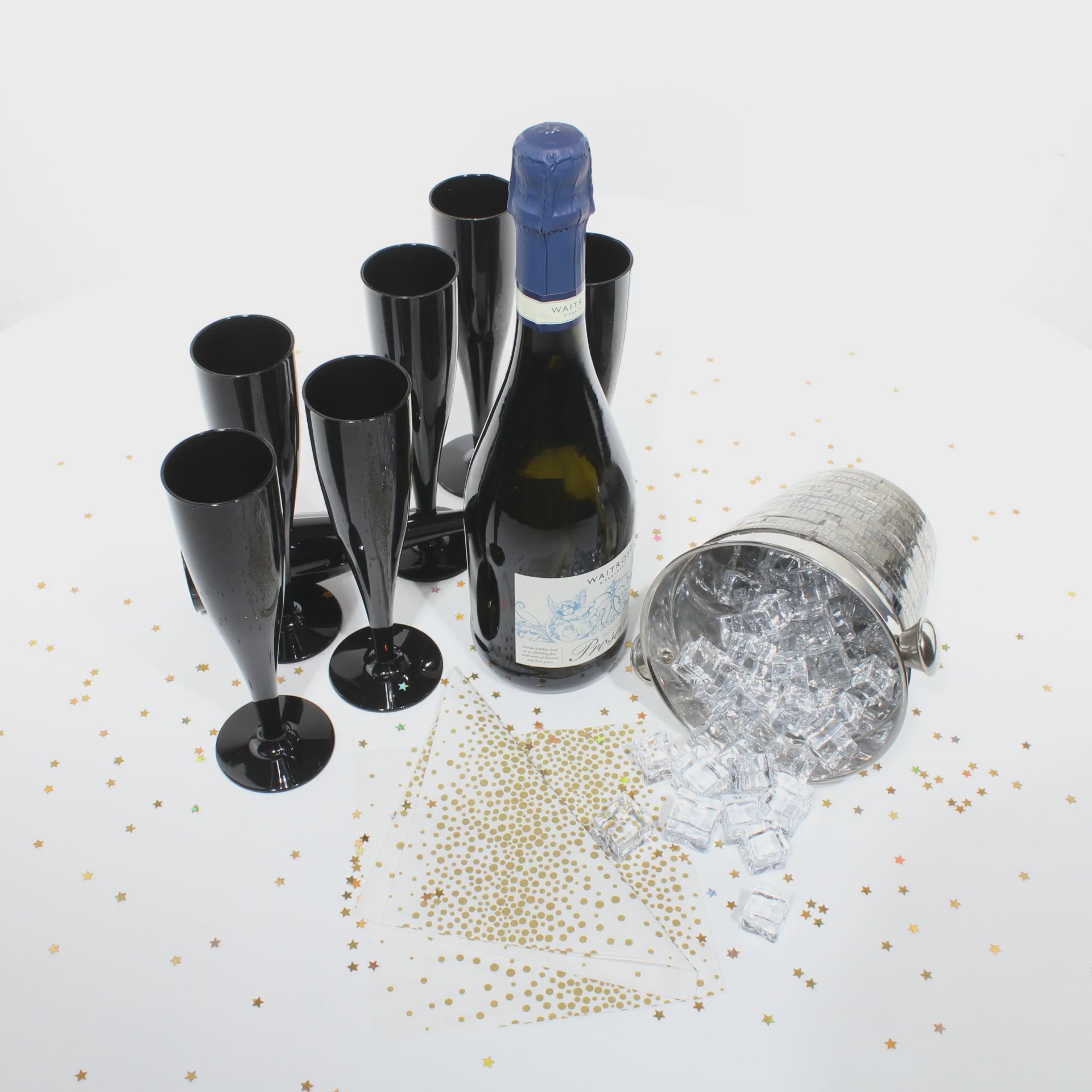 A video of several black champagne flutes with a bottle of prosecco, an ice bucket with ice cubes and gold glitter sprinkled on the table surface