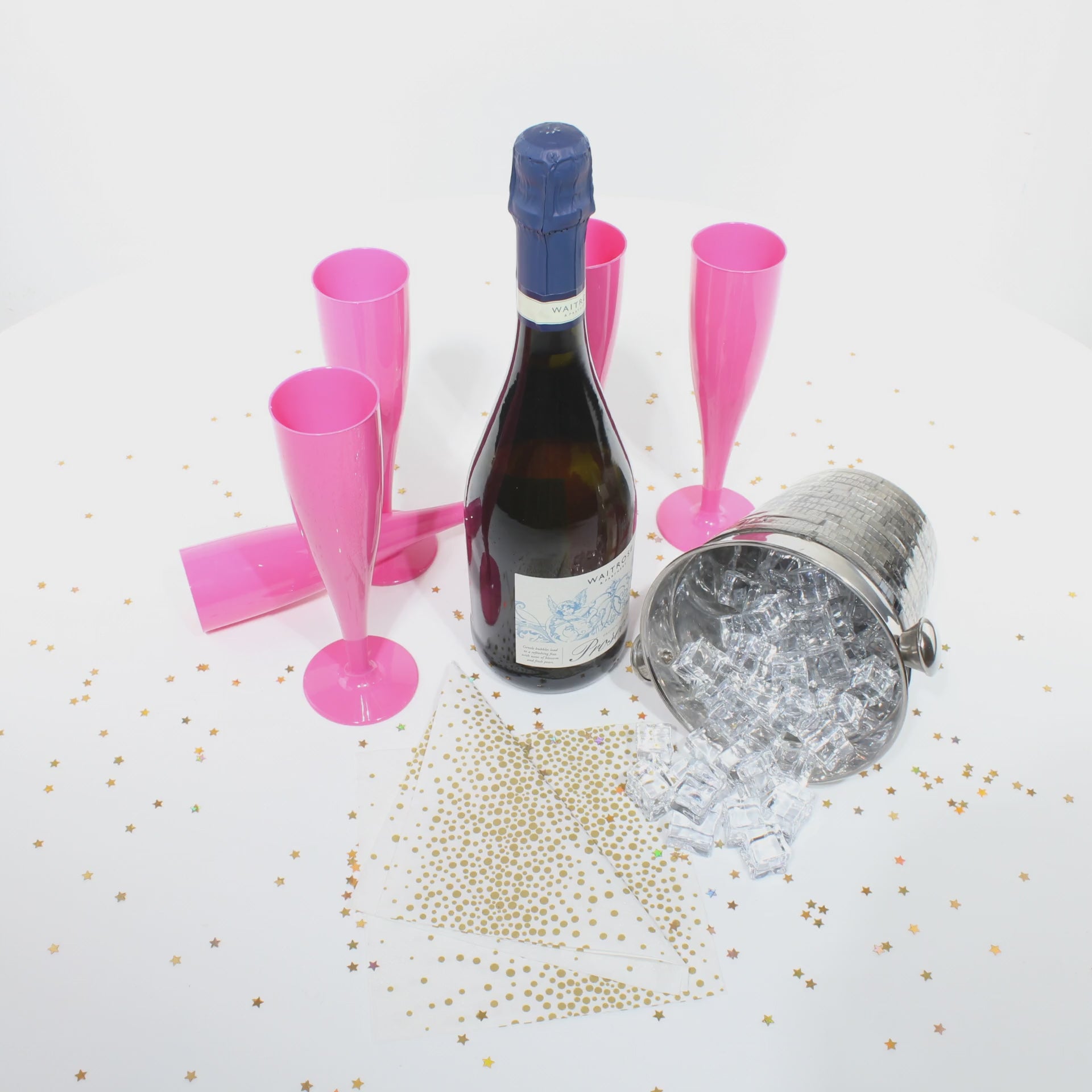 A video of several pink champagne flutes with a bottle of prosecco, an ice bucket with ice cubes and gold glitter on the table